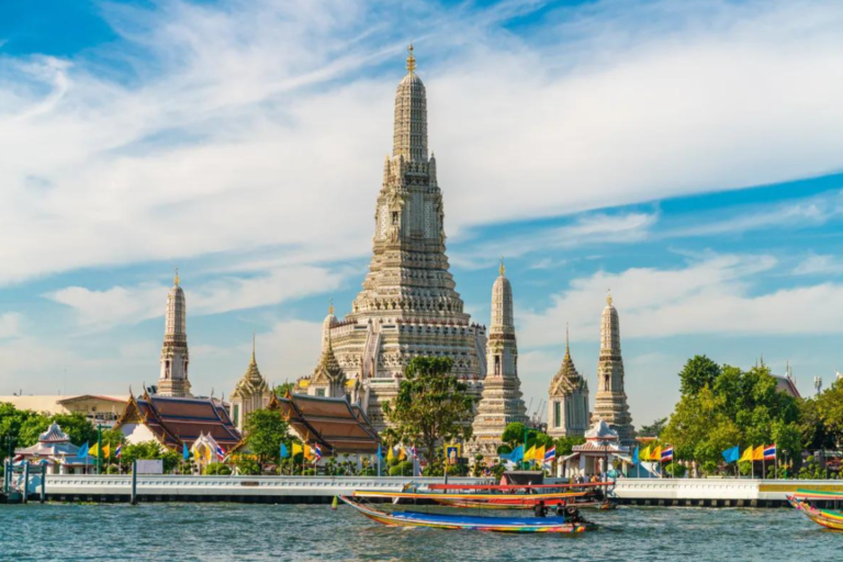 Wat Arun temple rising above the Chao Phraya River as long-tail boats pass through Bangkok.
